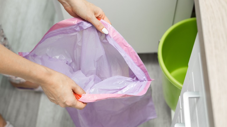 Açık bir mor çöp torbası açan bir kadın