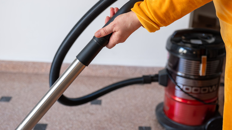 Vakum bağlantı hortumuna sahip bir karo zemini vakumlayan sarı bir kıyafetli bir kadın.