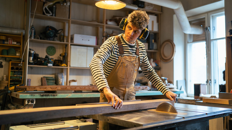 bir masa testeresi ile bir parça odun kesen kişi