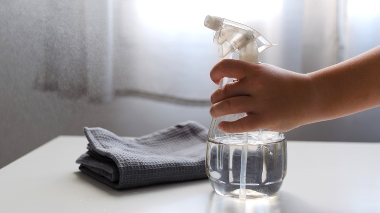 Kişi Gri kumaşın yanındaki masada oturan şeffaf sıvı içeren şeffaf sprey şişesi