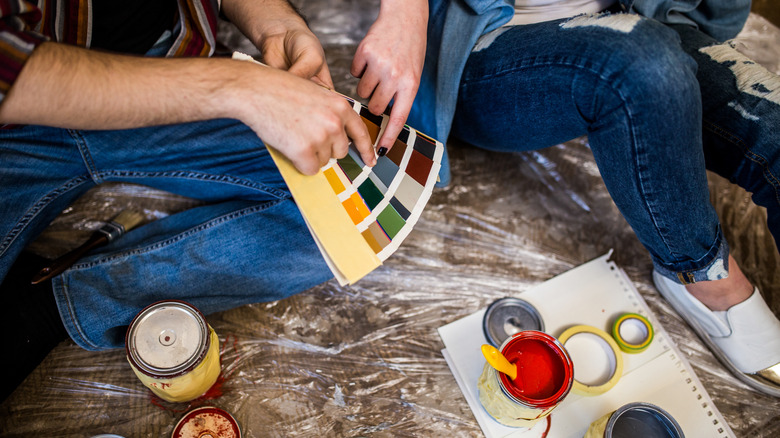 İki kişi renk renk örneklerine bakıyor ve bazı açık boya kutuları önlerinde oturuyor.