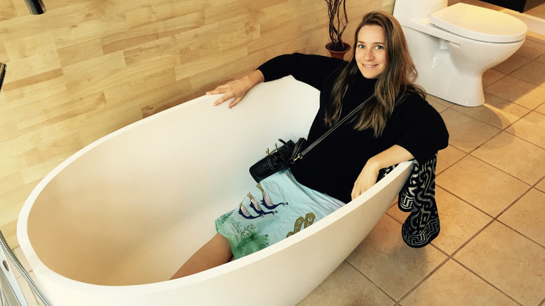 Gülümseyen bir kadın boş bir küvette oturuyor