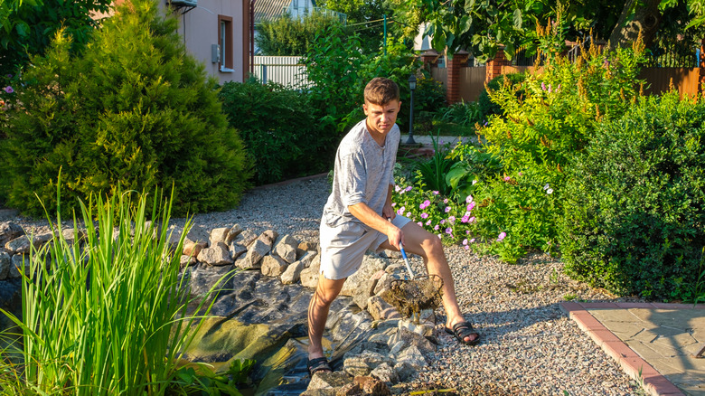 Bir ev sahibi, AA telli giysiler askıdan yapılmış bir ağ ile bahçe göletinden muck'i kepçe.