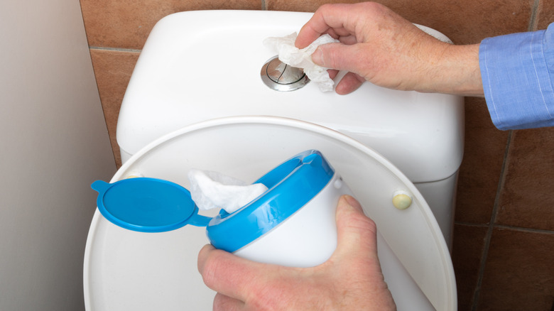 Tuvaletin temizleme düğmesini temizlemek için dezenfektan silme kullanarak el