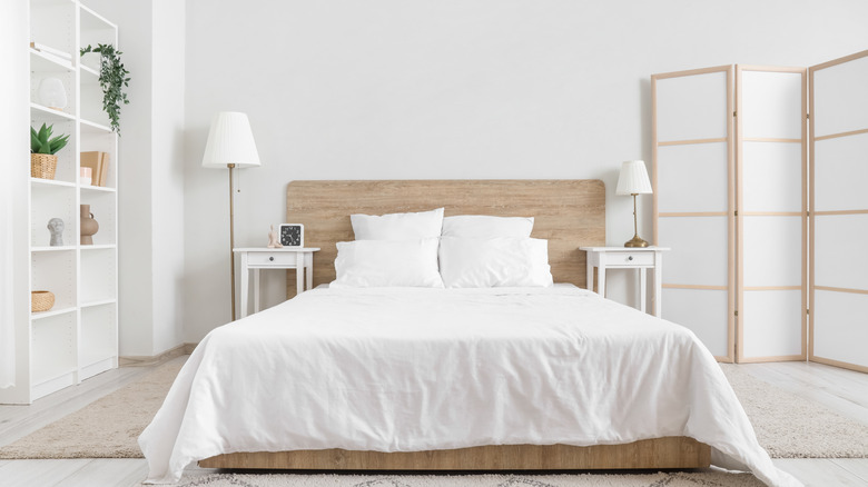 Beyaz yataklı yatak odası, köşede beyaz katlanır ekran ve bir kitaplık