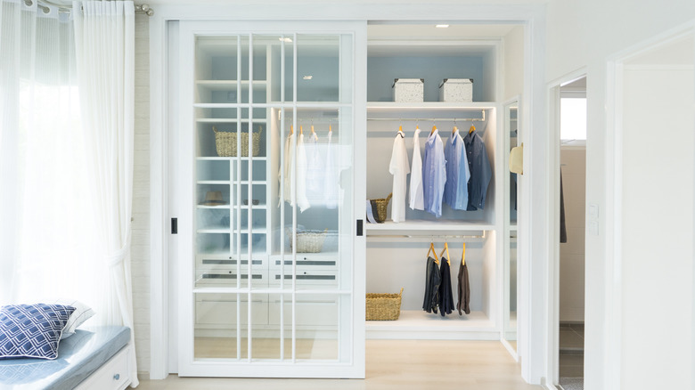 Düzgün asılı giysiler gösteren açık cam panel sürgülü dolap kapıları