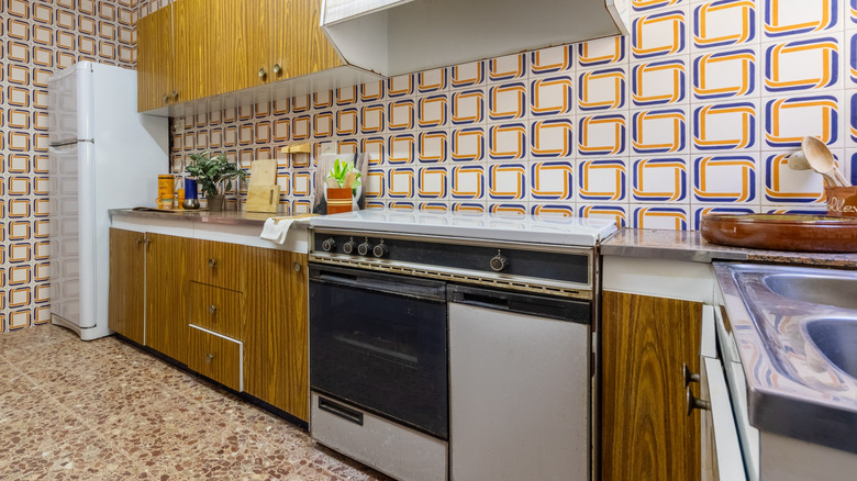 Yüksek sesle, fayans benzeri duvar kağıdı ve çatışan sahte taş döşeme ile çirkin bir mutfak.