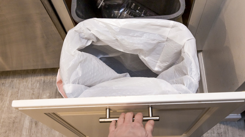 İçinde iki çöp kutusu ile bir çekmeceyi dışarı çeken biri