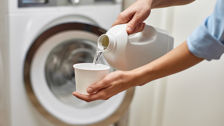 Eller çamaşır suyu bir çamaşır makinesinin önünde bir bardağa dökün