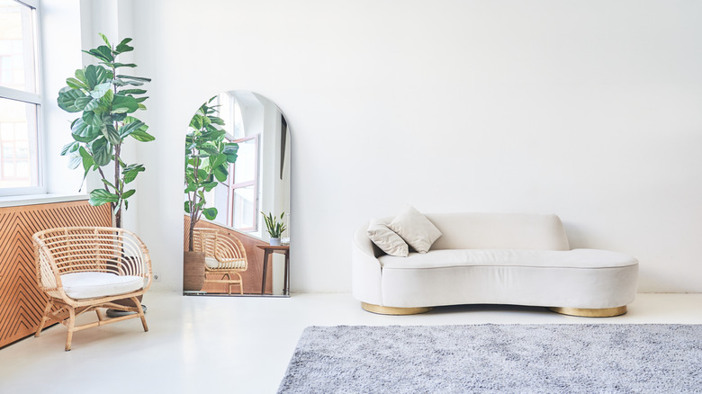 Beyaz kanepeli beyaz oda, rattan sandalye, ayna ve bitki