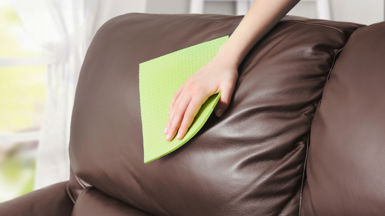 Sarı bir bezle koyu deri kanepeyi temizleyen kişi