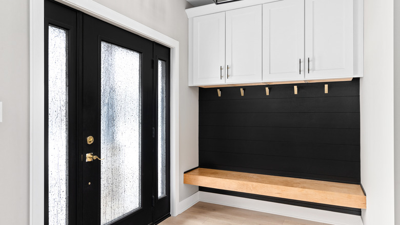 Tezgah oturma alanı, siyah gemi, beyaz dolaplar, altın ceket kancaları ve siyah ve altın ışık fikstürü olan modern bir çiftlik evi giriş yolu.