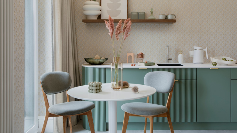 Cam vazo, mum, cam meyve kasesi ve tasarımcı su ısıtıcısı olan yuvarlak bir masada iki yastıklı sandalye