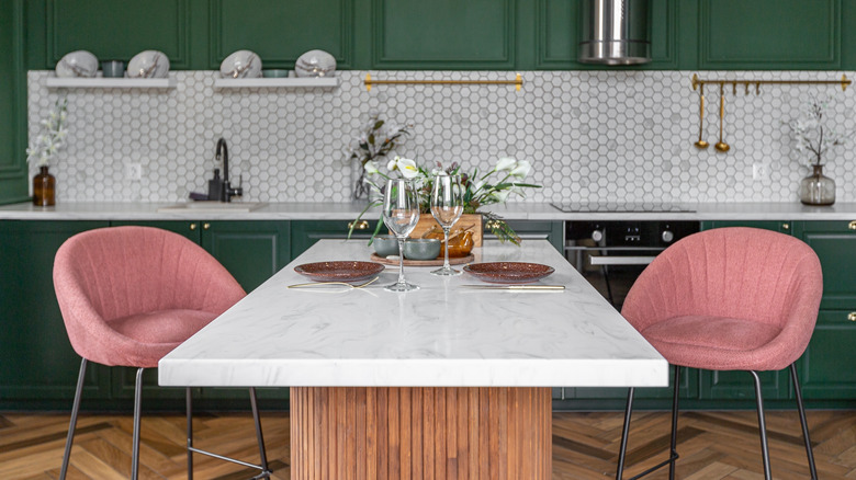 Orman yeşili bir mutfakta taştan yapılmış bir kahvaltı tezgahında iki pembe sandalye