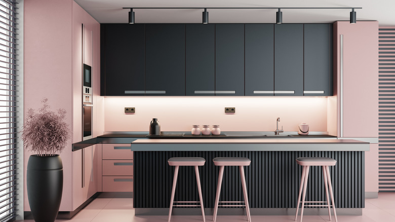 Siyah bir tezgahta siyah ve pembe dolaplar, pembe duvarlar ve pembe tabureler içeren bir mutfak