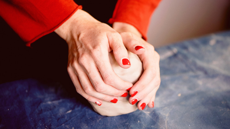 Parlak kırmızı tırnakları spor yapan bir çift açık tenli el, bir kil topunu yoğurur.