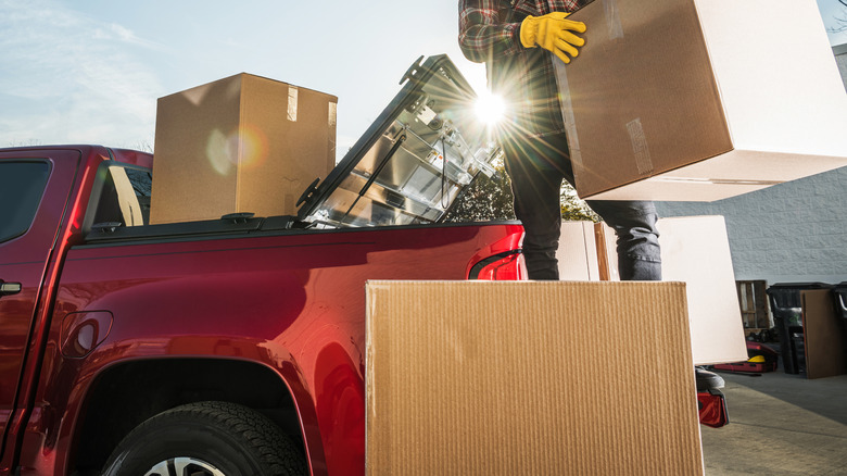 Sarı eldiven ve ekose gömleği olan bir adam tarafından kırmızı bir kamyonetin arkasına büyük kutular konuyor