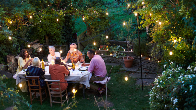Bir grup insan Cottagecore'dan ilham alan bir bahçede açık bir masada oturuyor