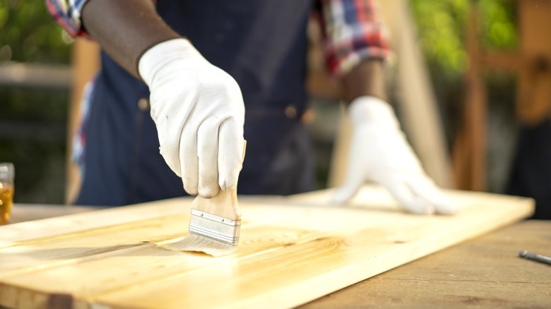 Beyaz eldivenlerde, çam tahtalarına ışık lekesini fırçalayan kişi