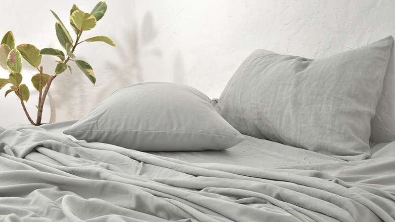 Arka planda bitki bulunan bir yatakta gri keten çarşaflar