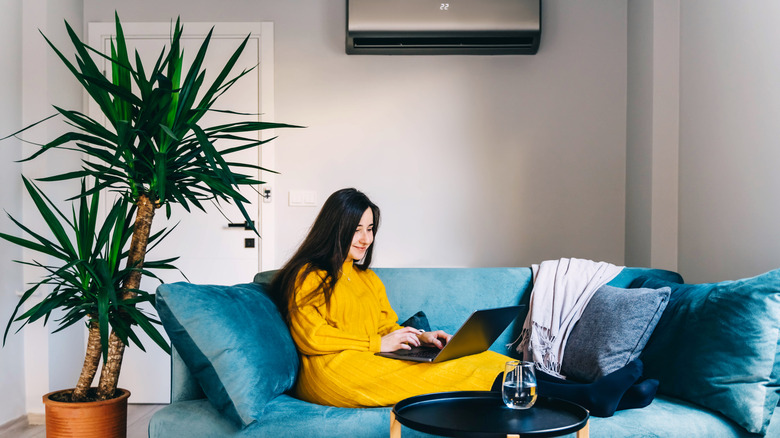 Dizüstü bilgisayarında kanepede oturan kadın arka planda klima