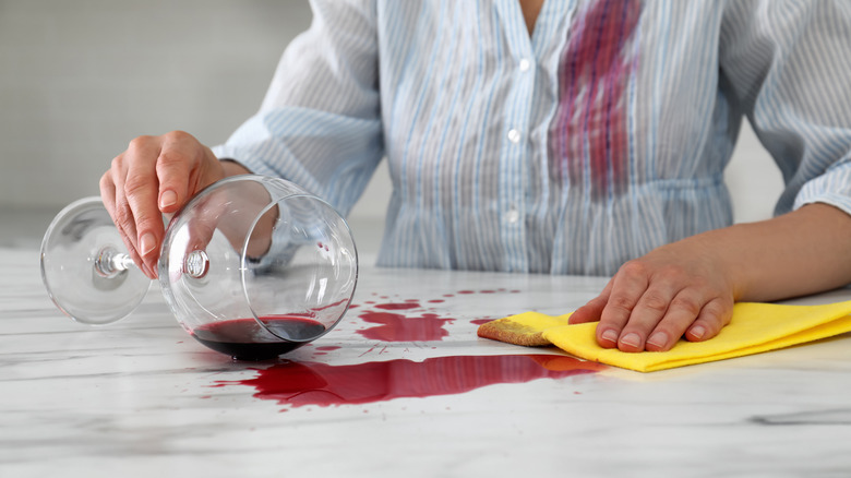 Beyaz mermer tezgah üzerine dökülen kırmızı şarabı temizleyen bir kişi