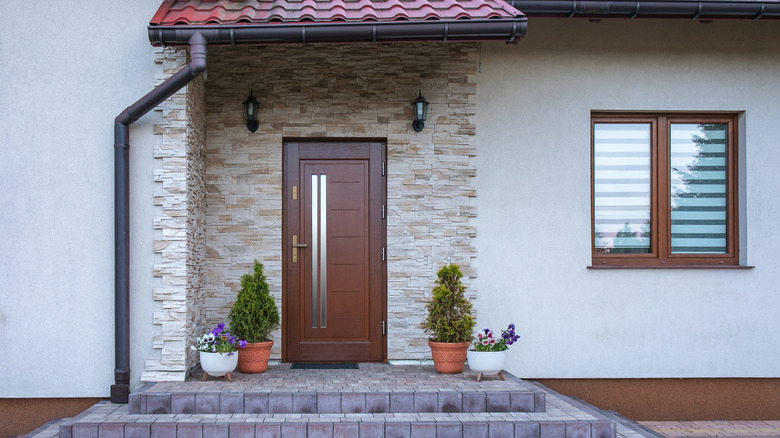 Aynı zamanda eşleşen ahşap döşeme olan bir pencereye sahip taş bir evde basit ama zarif kahverengi ahşap bir kapı.