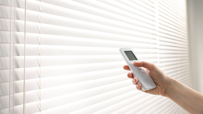 Beyaz panjurlarda bir uzaktan kumandayı işaret eden bir kişi