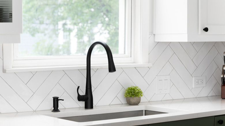 Siyah lavabolu beyaz bir mutfakta monte edilmiş beyaz bir balıksırtı desen backplash