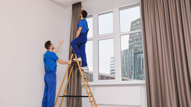 Mavi kıyafetlerde iki adam ağır perdelik asmak