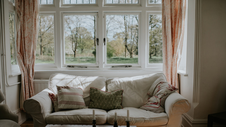 Açılan zemin uzunluğu perdeleri olan bir kanepe ve cumbalı pencereler