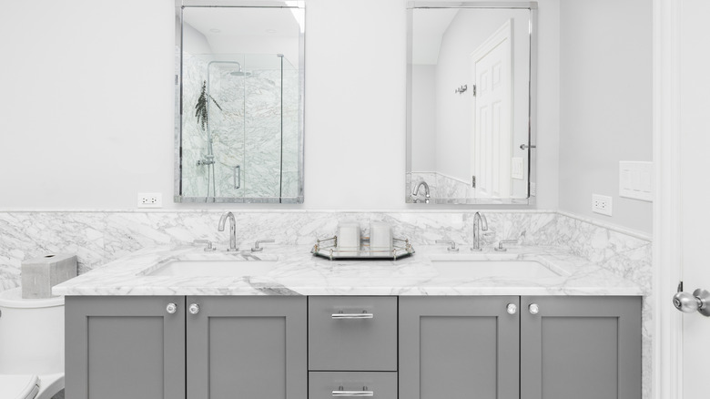 Mermer tezgahları ve gri dolapları olan bir banyo