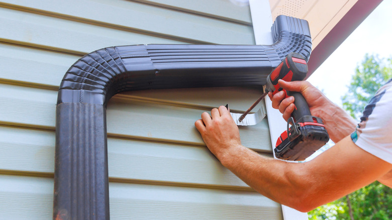 Bir kişi yağmur oluğu kurmak için bir matkap kullanır.