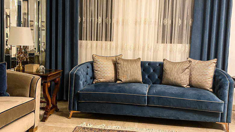 Temel olarak hafif, sıcak ahşap tonları olan mavi kadife bir kanepeye sahip lüks oturma odası.