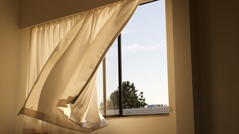 Açık garaj penceresinin önünde rüzgarda üfleyen perdeler