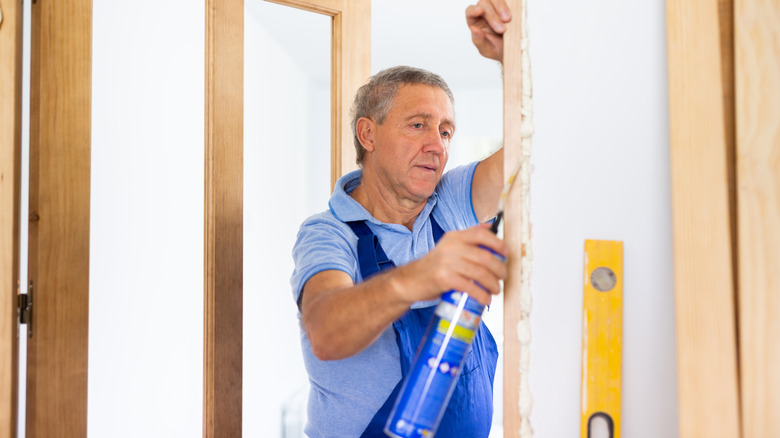 Mavi üniformalı orta yaşlı yüklenici kapı jambuna köpük sızdırmazlık maddesi takma.