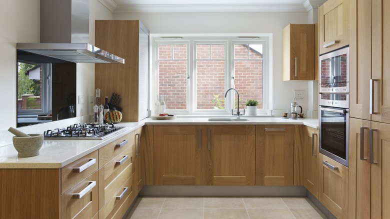 Meşe takılmış dolaplar ve çekmeceler ve krem renkli granit iş üstü olan modern bir dairede güzel bir mutfak.