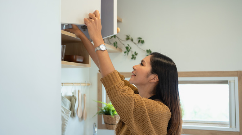 Bir kadın bir şeyi almak için yüksek bir dolaba ulaşır