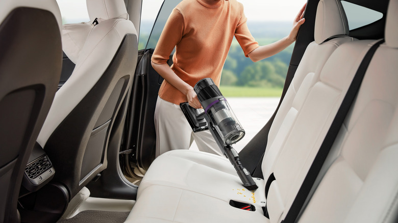 Arabadan kırıntıları temizlemek için el vakumu kullanan bir kişi