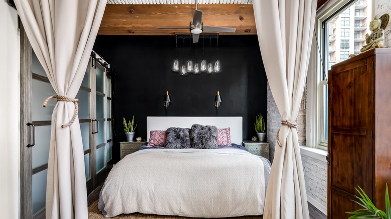 Beyaz yatak ve ahşap kirişli yatağın üstünde siyah duvar