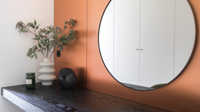 Yuvarlak ayna ve rafın arkasında turuncu duvar