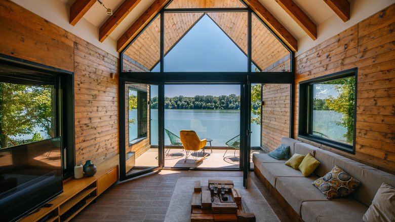 Bir göle bakan sırılsıklam ahşap duvar ve kirişli oturma odası