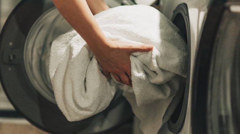 Çamaşır makinesine beyaz havlu yükleyen kollar
