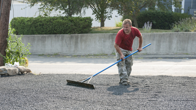 Bir çakıl yolunu düzeltmek için araç kullanan adam