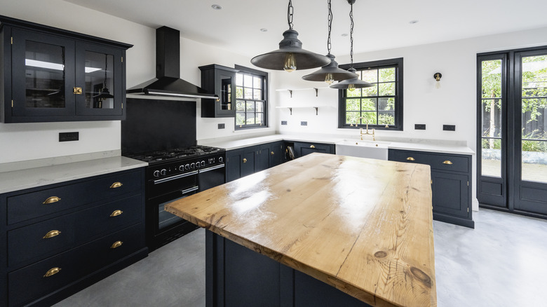 Siyah dolaplı bir mutfak, beyaz çevre tezgahı ve odun tepesinde bir ada