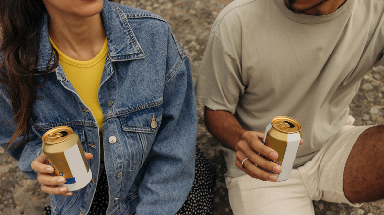 İki kişi içtikçe soda kutuları tutar.