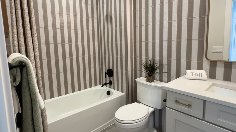 Duvarlarda taupe ve beyaz çizgili fayanslı bir banyo