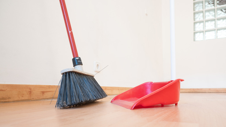 Duvara yaslanan bir süpürge, çöp kutusunun yanında.