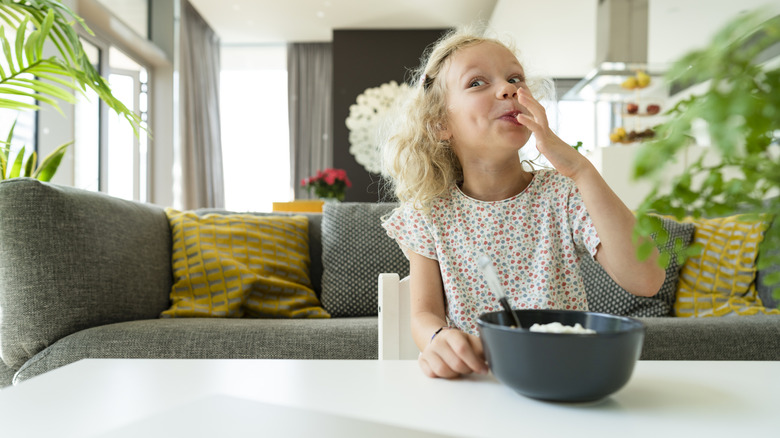 Küçük bir kız oturma odasında atıştırmalık yiyor