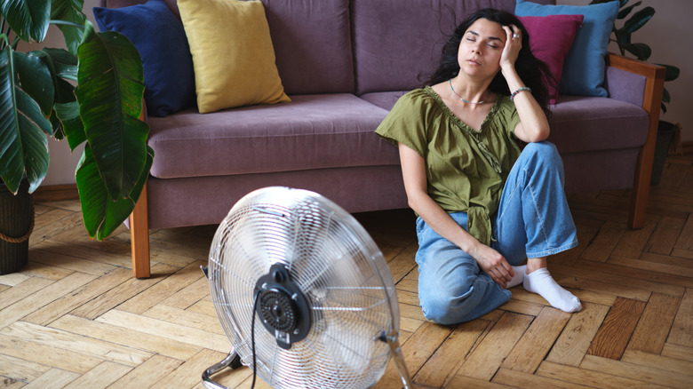 Elektrikli fan önünde yerde oturan yorgun bitkin genç kadın, ısı dalgası sırasında ferahlatıcı serinledi.